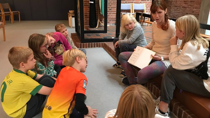 Børn og voksne sidder i en kreds og ser på en bog