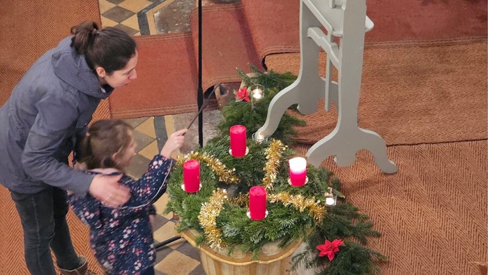 Eine Frau und ein Kind zünden Kerzen an einem Adventskranz an.