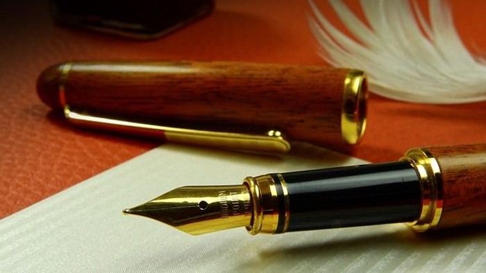 En pen med guld og mørk brune elementer ligger på papir ved siden af en hvid fjer.