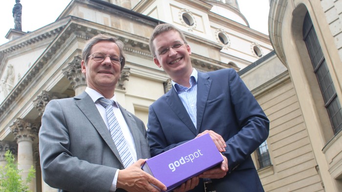 Zwei Männer in Anzügen halten eine lila Box mit 
