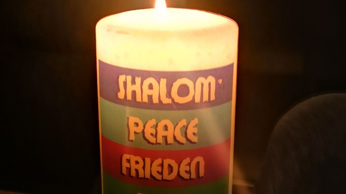 Das Bild zeigt eine Kerze mit der Aufschrift Schalom, Peace und Frieden. 