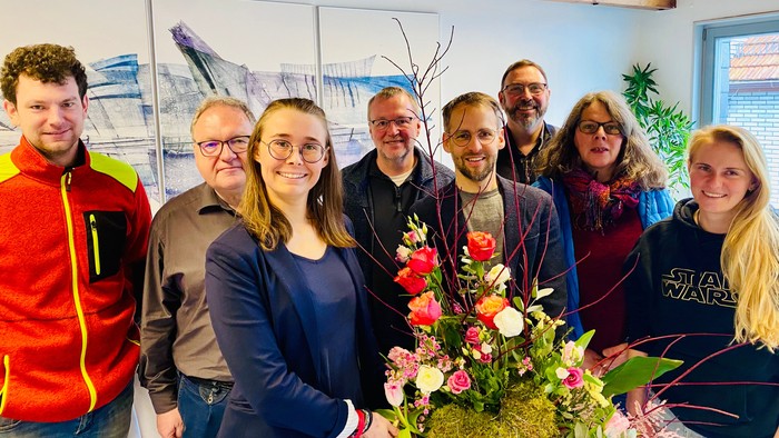 Gruppe von Personen, die in einem Büroumfeld mit Blumen posieren.