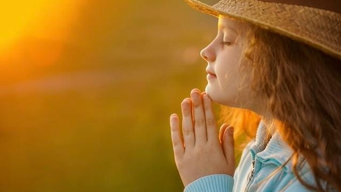 Ein Mädchen mit Strohhut betet im Sonnenuntergang.