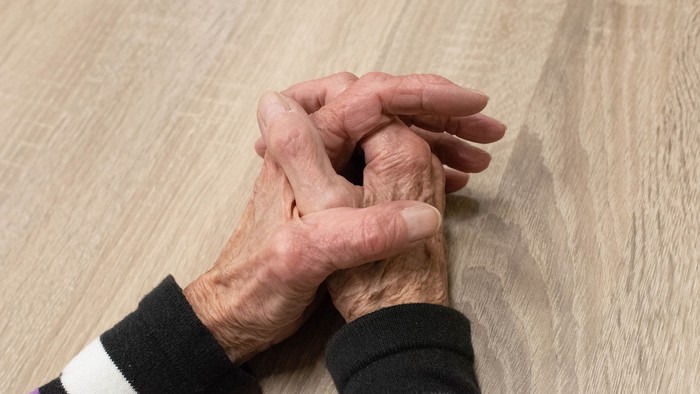 Zwei Hände halten sich auf einem Holzboden