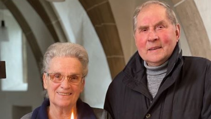 Paar steht hinter einem Tisch mit Blumen und einer angezündeten Kerze.