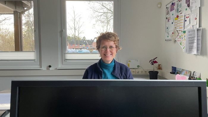 Frau an Schreibtisch vor Monitor und Fenster stehend