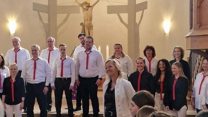 Eine Gruppe von Menschen singt in einer Kirche vor einem Kruzifix