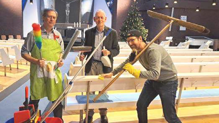 Drei Männer posieren verspielt mit Putzutensilien in einer festlichen Indoor-Veranstaltungsumgebung.