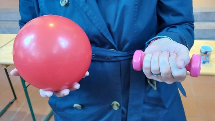 Person hält einen roten Ballon und eine rosa Hantel in den Händen.