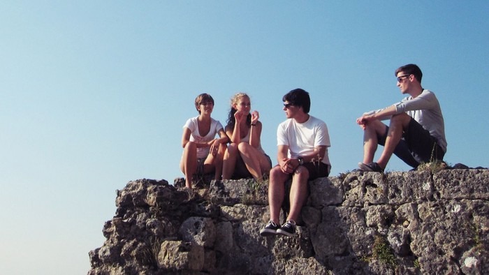 Vier Freunde sitzen gemeinsam auf felsigem Gelände unter einem klaren blauen Himmel.