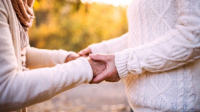 Zwei Personen halten sich an den Händen in einer parkähnlichen Umgebung.