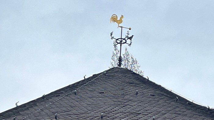 Das Bild zeigt ein Ziegelgebäude mit einem Wetterfahne auf dem Dach.