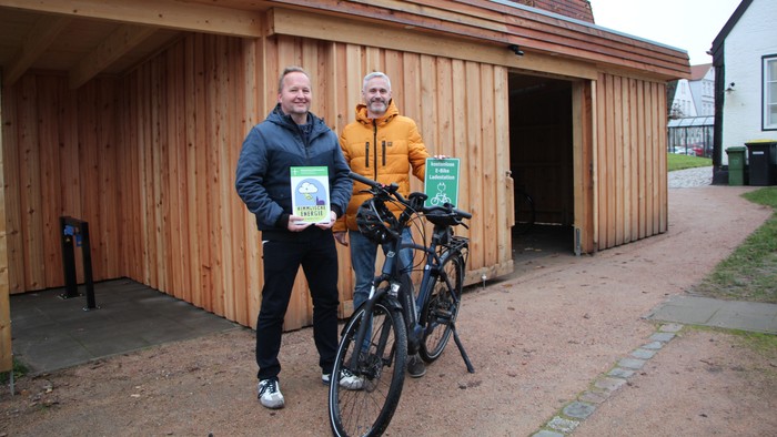 Zwei Personen mit Fahrrädern vor Holzgebäude