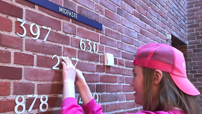 Pigen med rosa kappe og hat lægger et papir på mur med tallene 397, 630, 257 og 878.