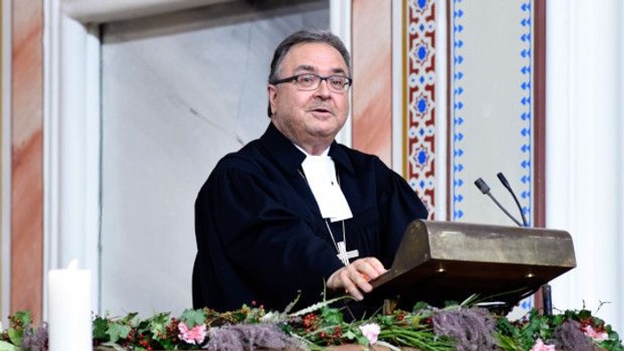 Ein Priester steht hinter einem Pult und hält ein Mikrofon.