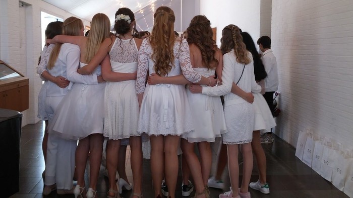 En gruppe piger i hvide tøjer og hvidt skmink står sammen i en rum.