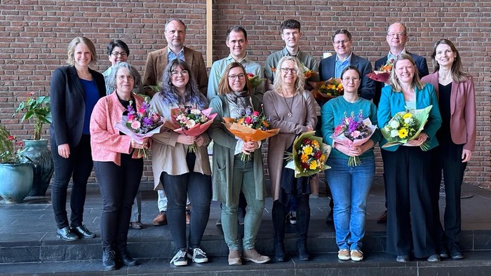 Eine Gruppe von Menschen posiert vor einem Kreuz, die Blumensträuße halten