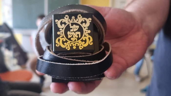Hand hält schwarze Gürtelschnalle mit goldenem Emblem in Raum