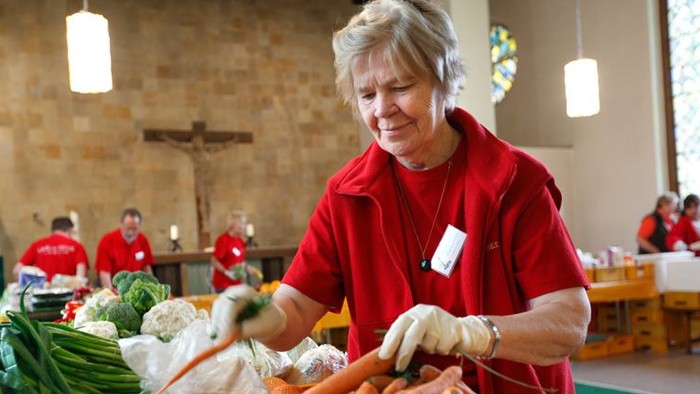 Frau in Rot verarbeitet Gemüse in einer Kirche.