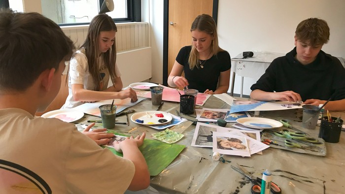 Fire unge sidder ved et bord og laver kunst.