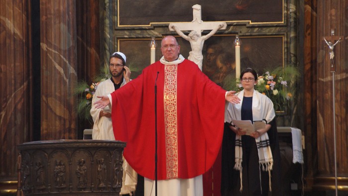 Ein Priester in roter Soutane steht vor einem Altar mit Kruzifix