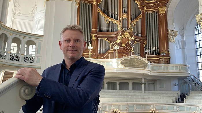 Mand i mørkt blå dragt står foran stor kirkeorgel