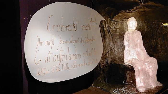 Die Ausstellung zeigt eine Figur und Texte in einer dunklen Umgebung.