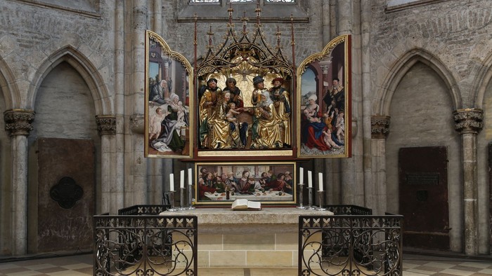 Das Bild zeigt einen Altar in einer gotischen Kirche mit aufwendigen Malereien und einem schmiedeeisernen Zaun.