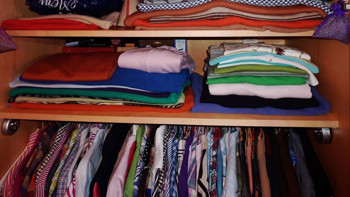 Ordentlicher Kleiderschrank mit farbenfroher Kleidung auf Regalen und Bügeln