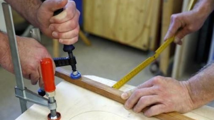 Zwei Personen arbeiten gemeinsam an einem Holzprojekt, eine verwendet einen Schrauber, die andere ein Lineal.