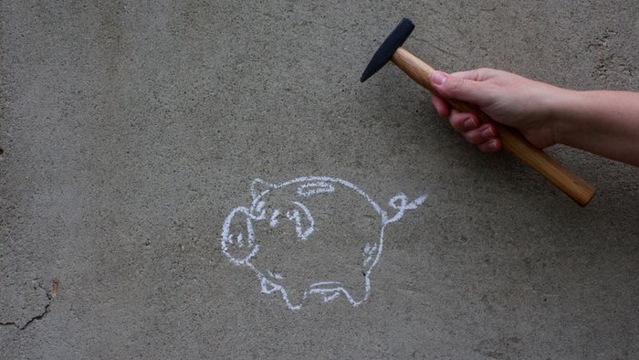 Hand hält Hammer über gemaltes Schweinchen mit Münze