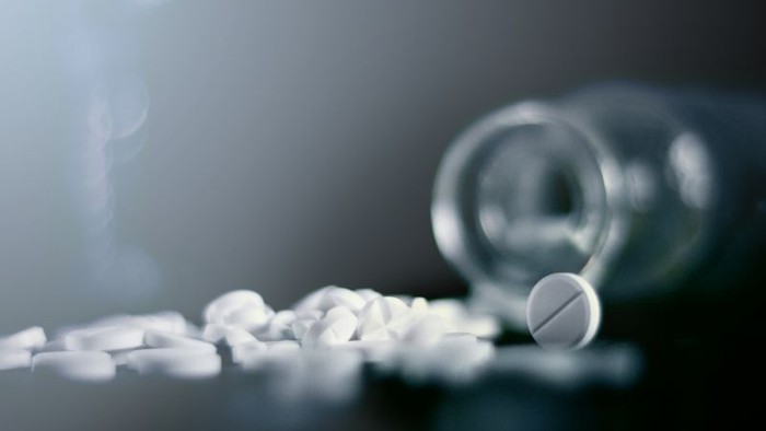 Einige Tabletten liegen neben einer durchsichtigen Flasche.