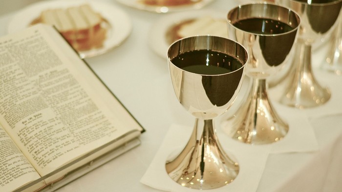 Drei silberne Kelche mit Rotwein auf Tisch, daneben offenes Buch und Teller mit Essen