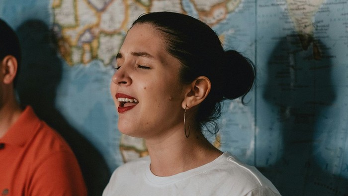 Eine junge Frau mit geschlossenen Augen und rotem Lippenstift lacht vor einer Weltkarte.