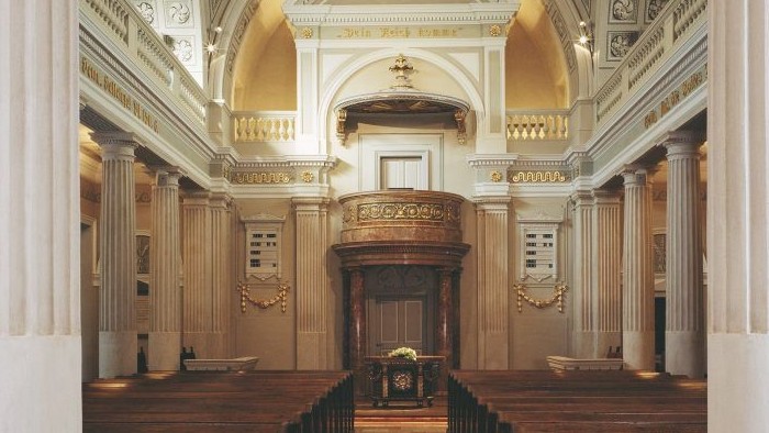 Großzügige Kirchenhalle mit hohem, verziertem Gewölbe und hölzernen Kirchenbänken