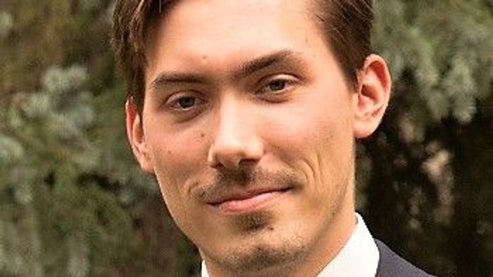 Junger Mann im Anzug mit Krawatte vor grünem Hintergrund.