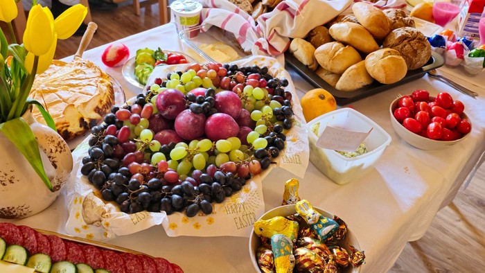Ein Tisch beladen mit verschiedenen Snacks und Obst, darunter Trauben, Erdbeeren, Gemüse und Brot.