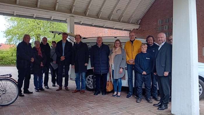 Eine Gruppe von Menschen steht unter einem Vordach vor einem Ziegelgebäude.