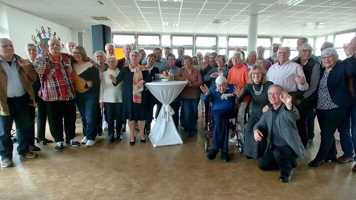Eine Gruppe von Menschen feiert bei einer Veranstaltung in einem Raum mit großen Fenstern.