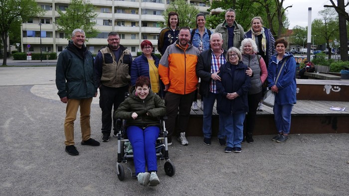 Eine Gruppe von Menschen posiert vor einem Gebäude, eine Person sitzt im Rollstuhl