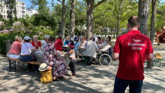 Eine Gruppe von Menschen versammelt sich im Freien in einem Park, wobei eine Freiwillige in Rot steht und mit dem Rücken zugewandt ist.