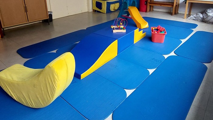 Ein Kinderzimmer mit blauen Matten, gelben Kissen und Spielzeug.