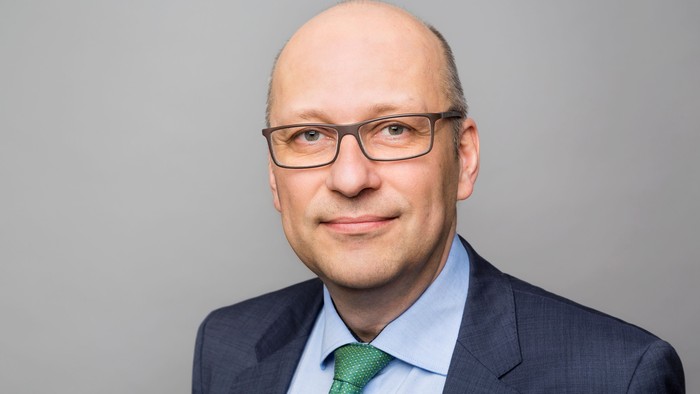 Mann im Anzug mit Brille und grüner Krawatte lächelt.