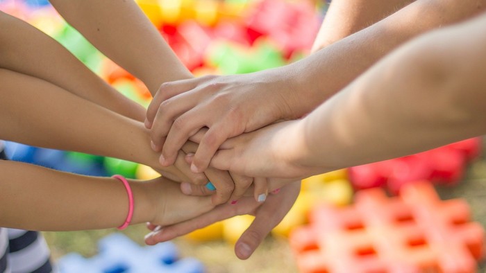 Viele Hände halten sich gegenseitig, farbenfrohes Hintergrundmuster