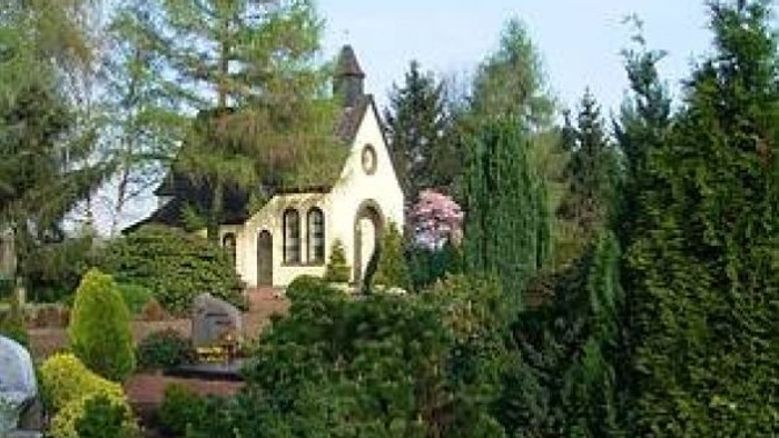 Ein kleines weißes Haus mit spitzem Dach inmitten eines grünen Gartens.