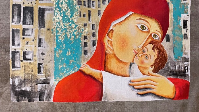 Ein Mutter mit rotem Kopftuch hält ein Kind im Arm, vor einem Stadtbild