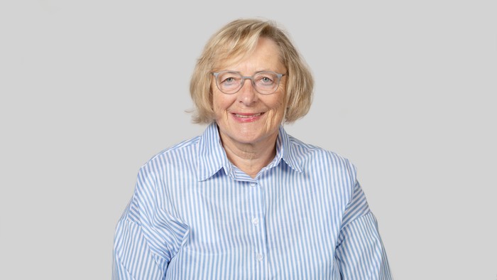 Eine ältere Frau mit Brille und gestreifter Bluse lächelt.