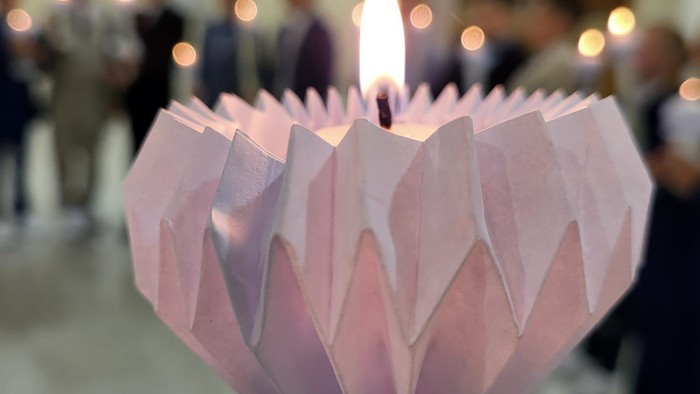 Eine rosa Origami-Laterne mit brennender Kerze in einem Raum voller Menschen
