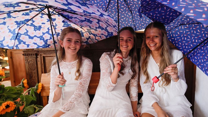 Tre pige i hvidt sitter under blå paraplyer