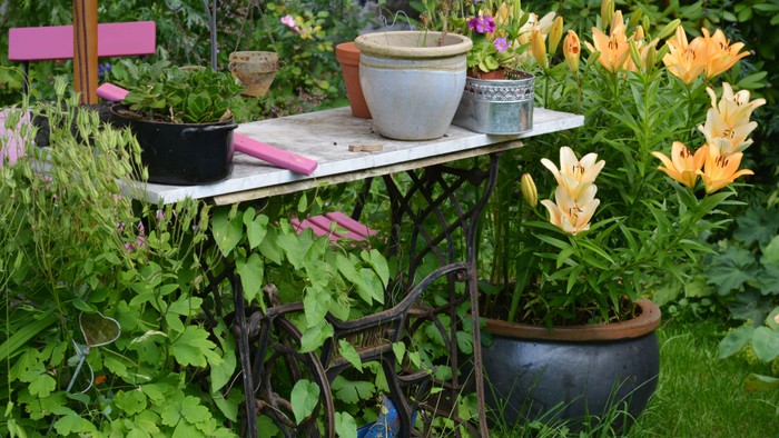 Ein kleiner Tisch im Garten mit Topfpflanzen und Gartengeräten.